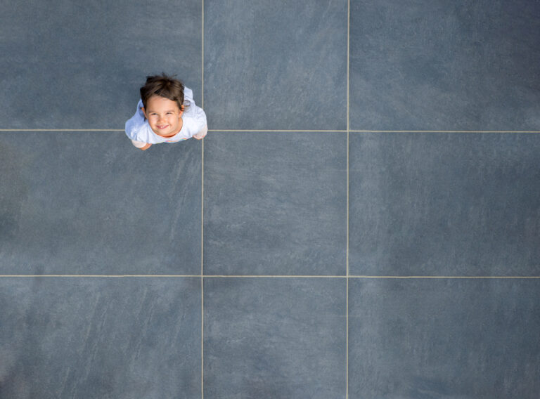 Child looking up from tiled floor, smile, young girl, playful, happy, indoor setting, modern tiles, casual, wide-angle shot.