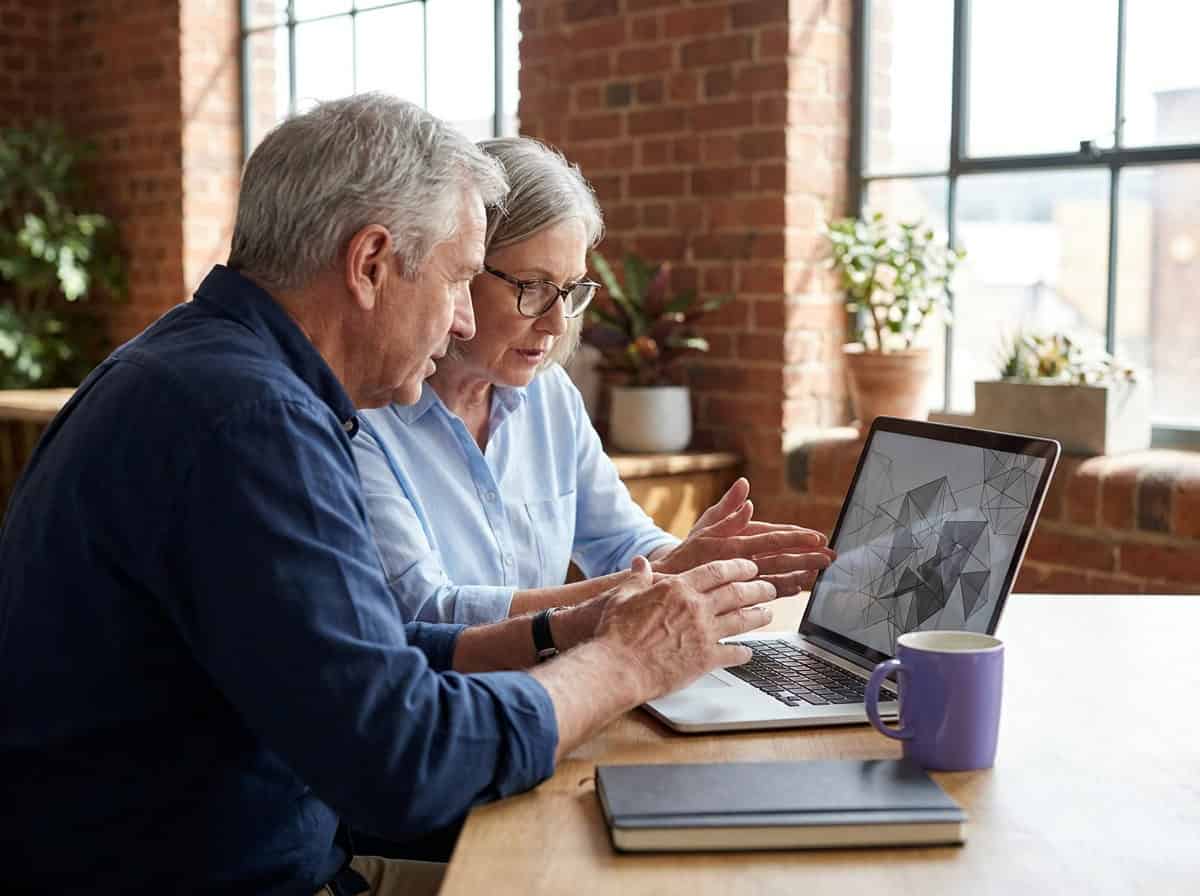 Two professionals gesture toward a laptop screen displaying a wireframe design in a sunlit brick office.