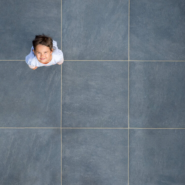 Child looking up from tiled floor, smile, young girl, playful, happy, indoor setting, modern tiles, casual, wide-angle shot.
